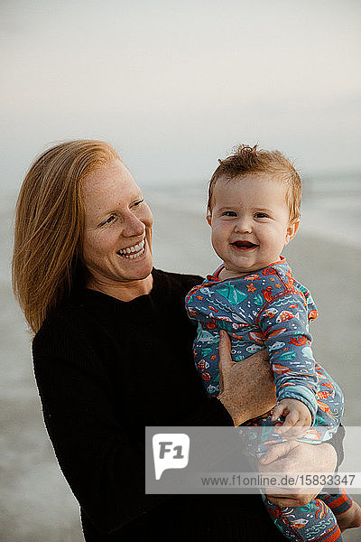 young redhead mom laughs and holds laughing fat baby boy in onesie