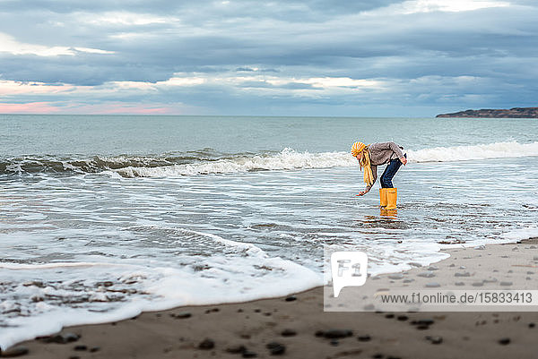 Preteen mit gelben Stiefeln holt Muscheln vom neuseeländischen Strand