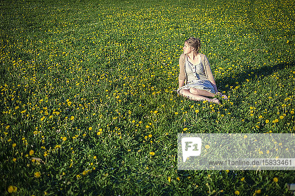 Junge Frau sitzt im frühen Frühling auf einem Löwenzahnfeld.