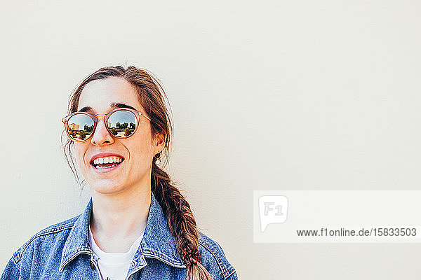 Nahaufnahme einer attraktiven jungen Frau  die mit Sonnenbrille auf pastellfarbenem Hintergrund lacht