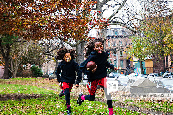 Sisters smiling while playing American football at park in city during autumn