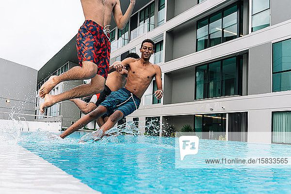 Drei Teenager springen in einen von Gebäuden umgebenen Pool