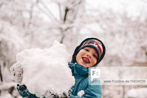 Happy boy sticking out tongue while playing with snow in winter