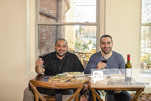 Zwei stolze Geschäftsinhaber sitzen zusammen an einem Restauranttisch mit Wein