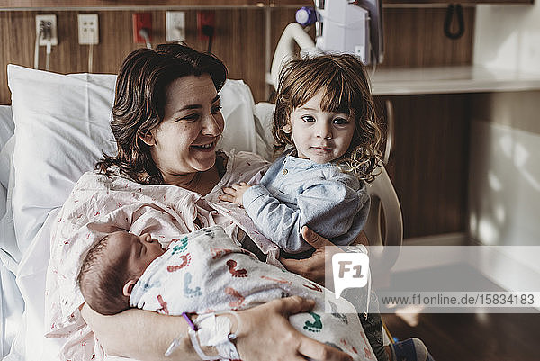 Mid view of mother holding newborn son meeting siblings