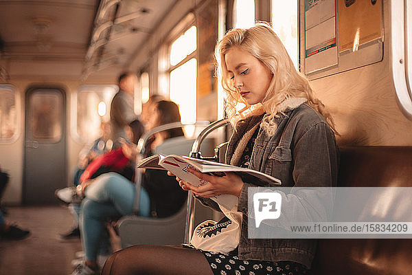 Young woman reading magazine while traveling in subway train