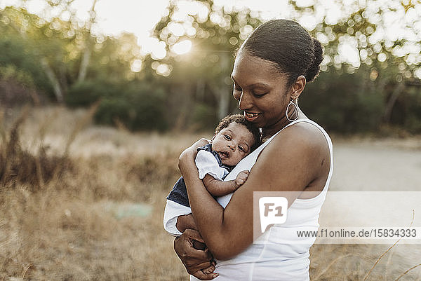 Porträt einer jungen Mutter  die ein Kleinkind hält  auf einem Feld im Hintergrund