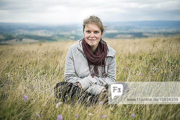 Young woman sitting in grassy meadow looking at camera