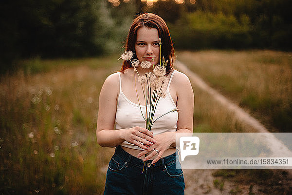 Junge Frau hält einen Strauss Löwenzahnblumen auf einer Wiese