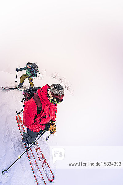 Zwei Personen beim Skitourengehen auf dem Gipfel im Nebel angekommen