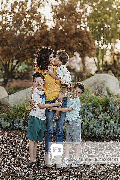 Porträt einer Mutter  die ihren Sohn küsst  mit Jungen  die sie im sonnigen Garten umarmen