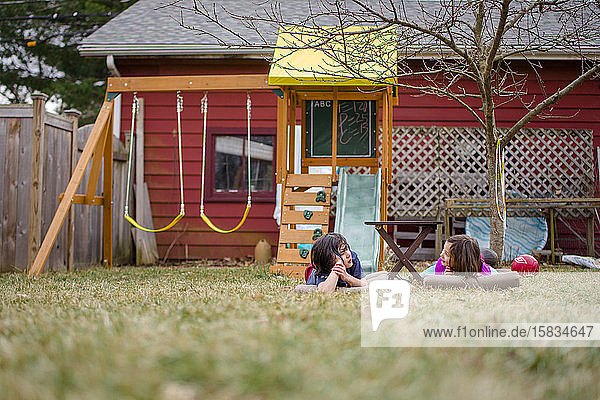 Zwei Kinder lagen im Gras im Hof und unterhielten sich mit einem Spielset im Hintergrund
