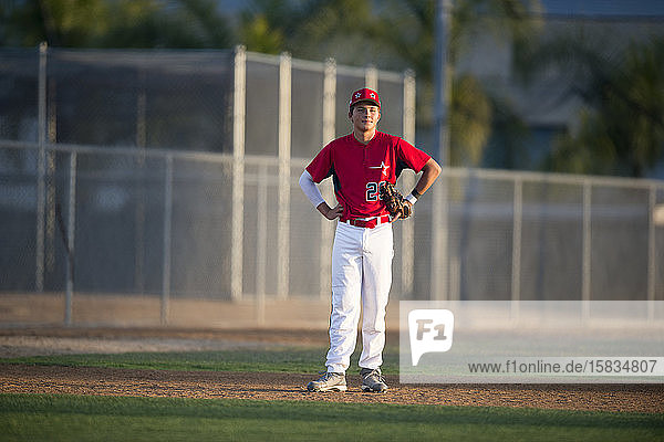 Teen baseball player in red uniform standing in the infield