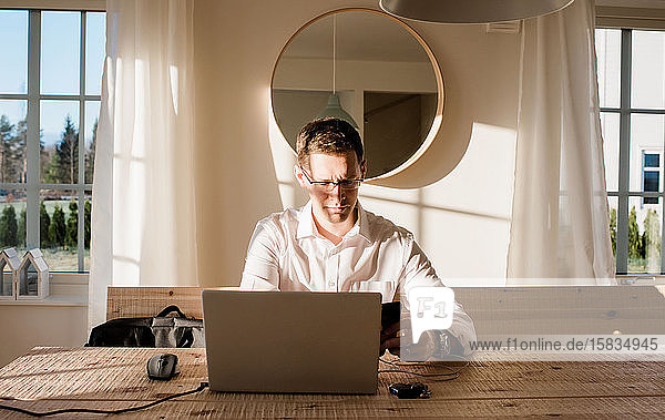 Mann arbeitet von zu Hause aus und schaut konzentriert auf sein Telefon und seinen Laptop