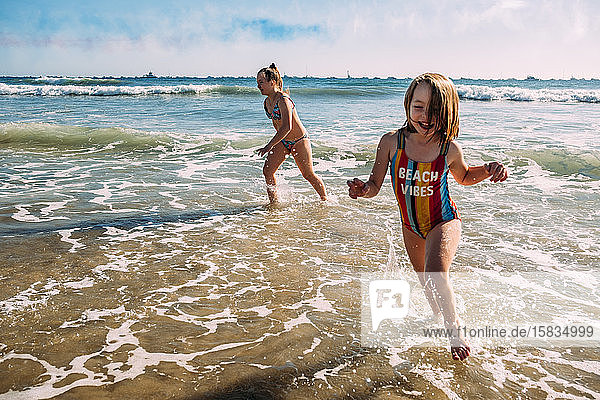 sisters running on beach and splashing in water
