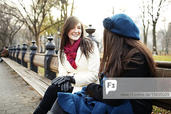 Friends sitting on bench in city park in winter