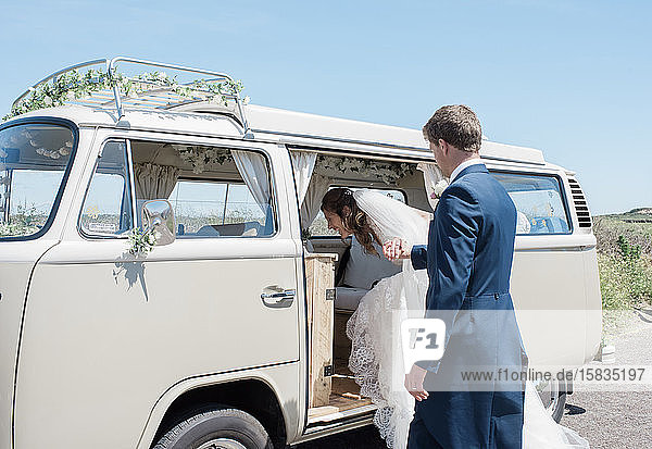 groom helping bride get into a camper van on their wedding day