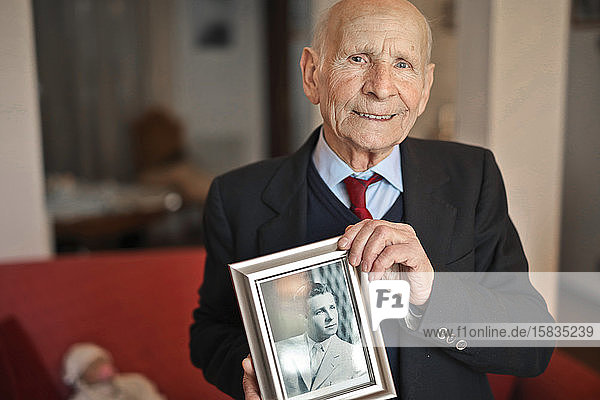 Porträt eines älteren Mannes mit einem Erinnerungsfoto als junger Mann