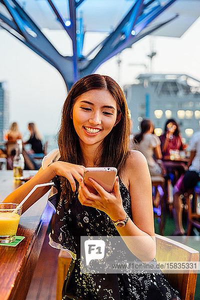 Thailändische Frau mit Telefon in der Rooftop Bar