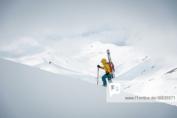 Eine Person geht mit Skiern auf dem Rücken auf einen Gebirgskamm