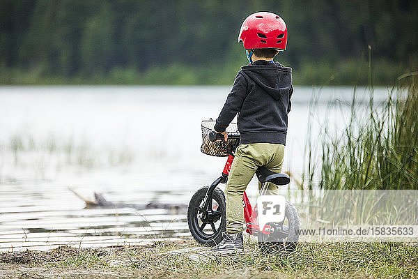 Rear view of young boy on balance bike at lakeshore.