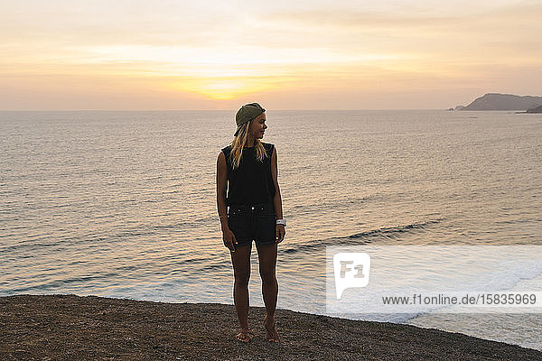 Young woman standing on rock at the beach at sunset