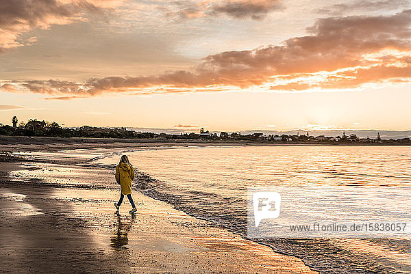 Mädchen geht bei Sonnenuntergang am neuseeländischen Strand spazieren