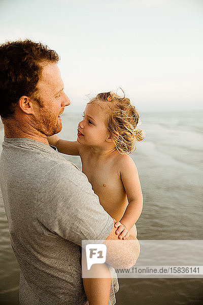 nacktes Mädchen schaut ihren Vater beim Strandspaziergang im Urlaub liebevoll an