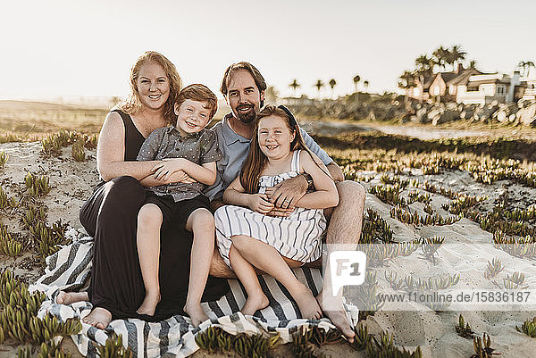 Portrait of family of four sitting on blanket at beach during sunset
