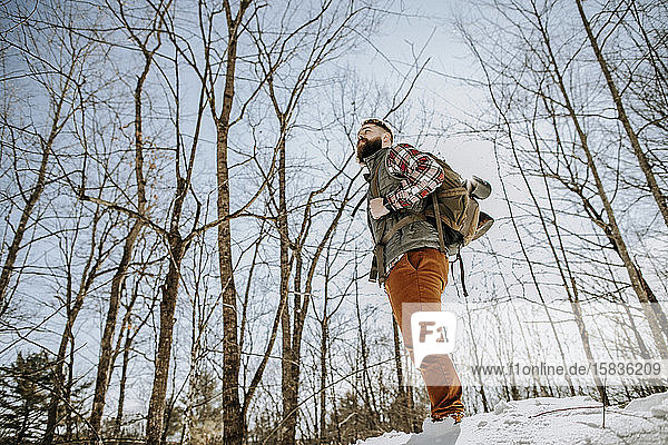 Man with flannel  beard and pack stands in snow in woods in winter