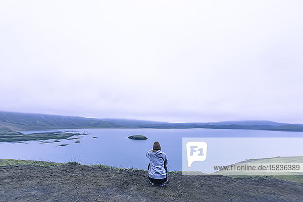 Frau sitzt und fotografiert einen See im isländischen Hochland bei Sonnenuntergang