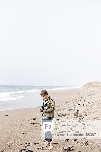 Junger Mann steht am Strand und fotografiert mit einer Filmkamera