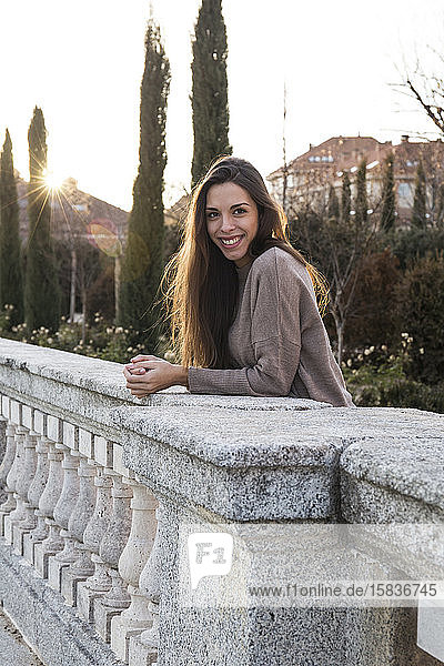 smiling young woman leaning on a stone bridge