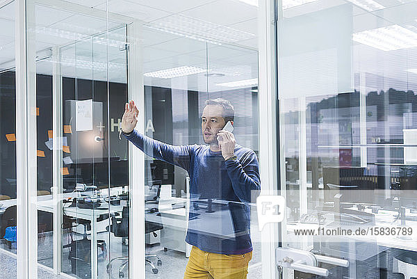 Seitenansicht eines Geschäftsmannes  der mit einem Smartphone spricht  während er an einer Bürowand steht