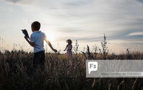 Geschwister spielen draußen bei Sonnenuntergang mit Papierfliegern zusammen