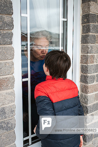 Junge  der während der Covid-19-Pandemie durch das Fenster zur Oma schaute.