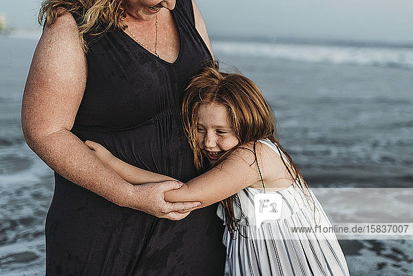 Seitenansicht einer glücklichen jungen Tochter  die ihre Mutter in der Abenddämmerung im Meer umarmt