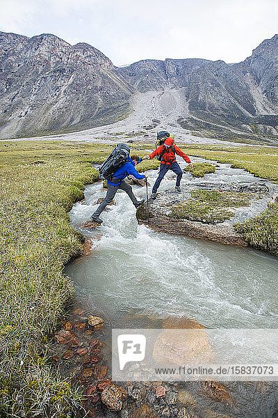 Backpackers help one another cross a river in Akshayak Pass.