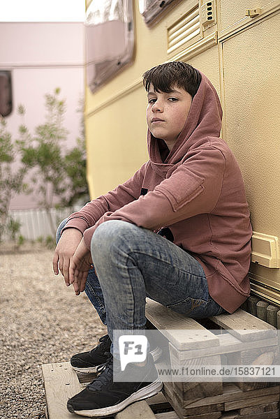 Porträt eines jungen Teenagers  der vor einem Wohnmobil sitzt und in die Kamera schaut