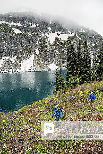A man and women hike around a beautiful alpine lake on a cloudy  rainy summer day in the Coast Mountains around Pemberton  British Columbia.