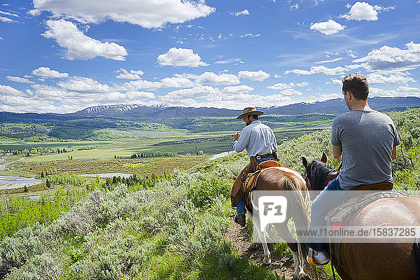 Zwei Männer reiten auf Pferden  hoch oben auf einem Berg  unten im Tal