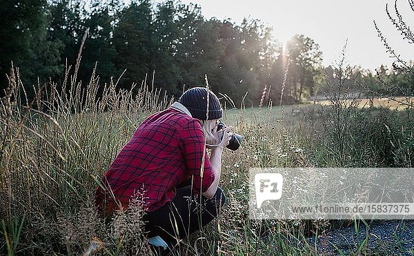 Frau  die im Sommer ein Foto von Wildblumen auf einem Feld macht