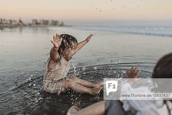 Glückliches 2-jähriges Mädchen planscht am Strand im Meerwasser