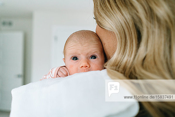Over the shoulder view of a newborn baby girl being held by her mom
