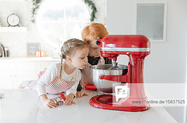 Zwei Kleinkinder backen Weihnachtsplätzchen und schauen in einen Mixer