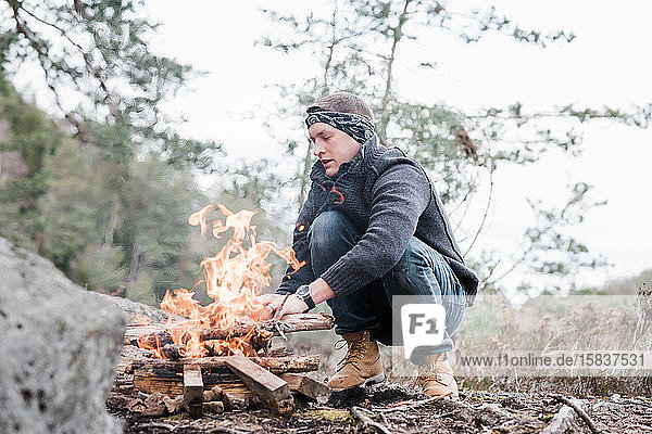 Mann legt in Schweden Stöcke an ein Lagerfeuer im Freien
