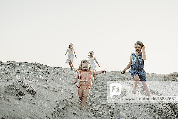 Vier junge Schwestern rennen und spielen im Sand bei Sonnenuntergang am Strand