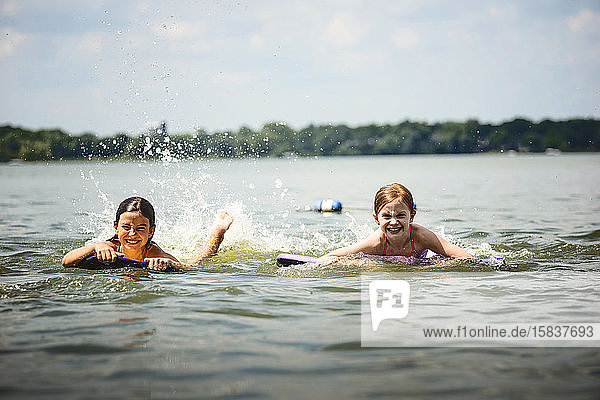 Zwei junge Mädchen in Badeanzügen auf Kickboards in einem See