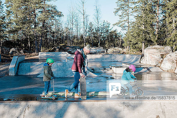 Mama und ihre Kinder laufen mit Fahrrädern und Rollern über einen Skatepark