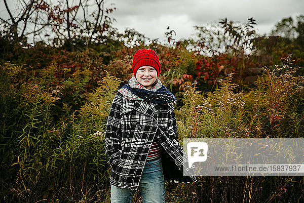 Teenager-Mädchen mit rotem Hut steht lächelnd auf einem herbstlich gefärbten Feld